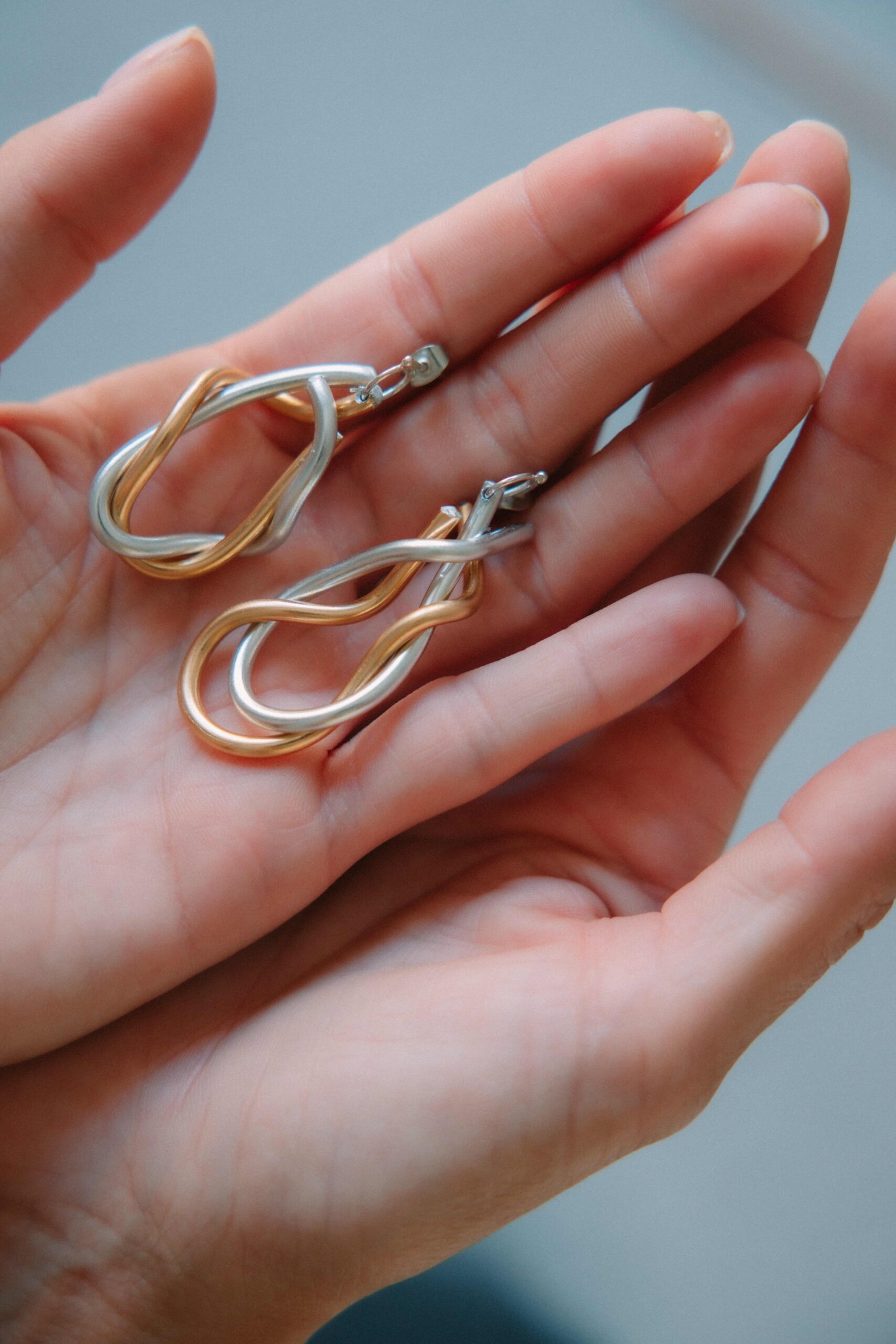 AGKALIA silver and gold knotted earrings held in the hand