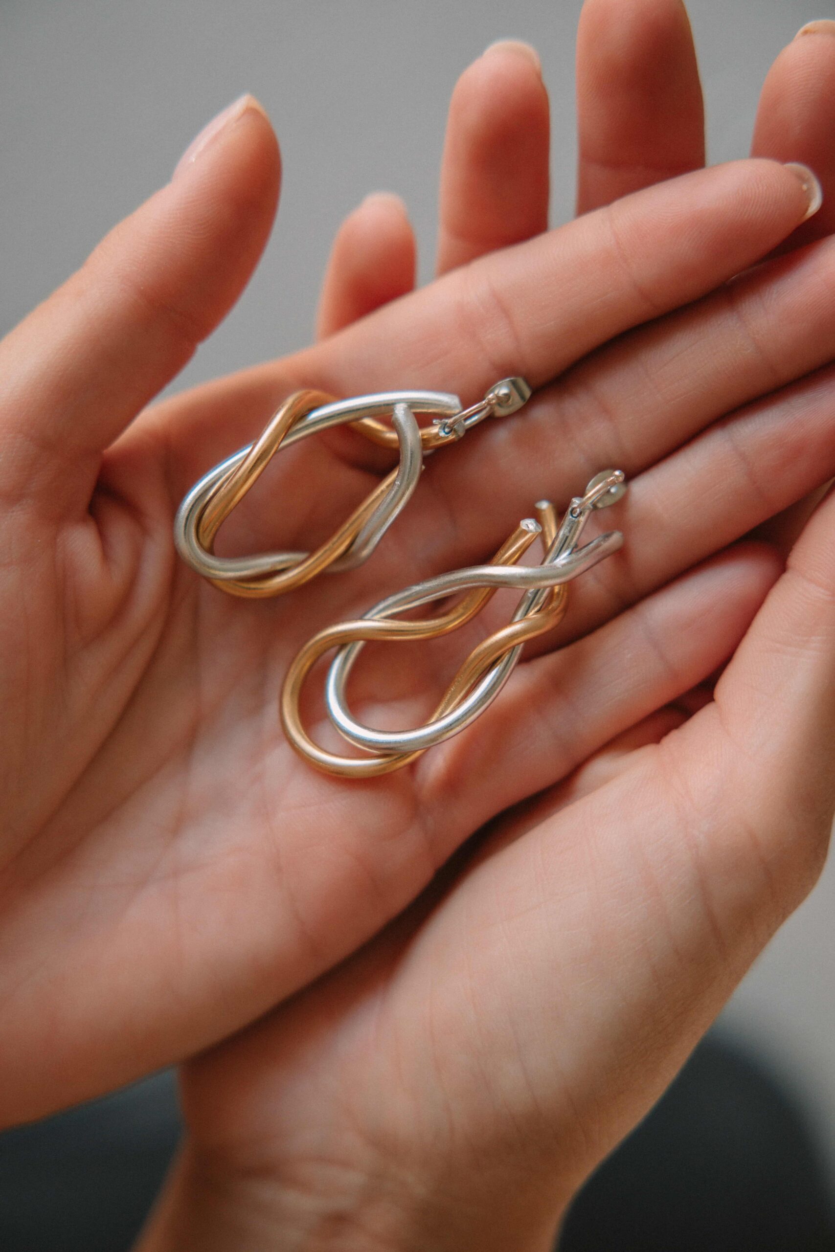 AGKALIA silver and gold earrings held in both palms